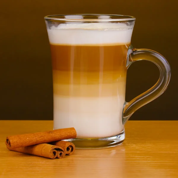 Latte Machiato im Glas mit Henkel mit Milchschaum und Zimtstangen