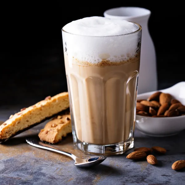 Latte Machiato im Glas mit Milchschaum, Brot, Mandeln und Löffel im Hintergrund